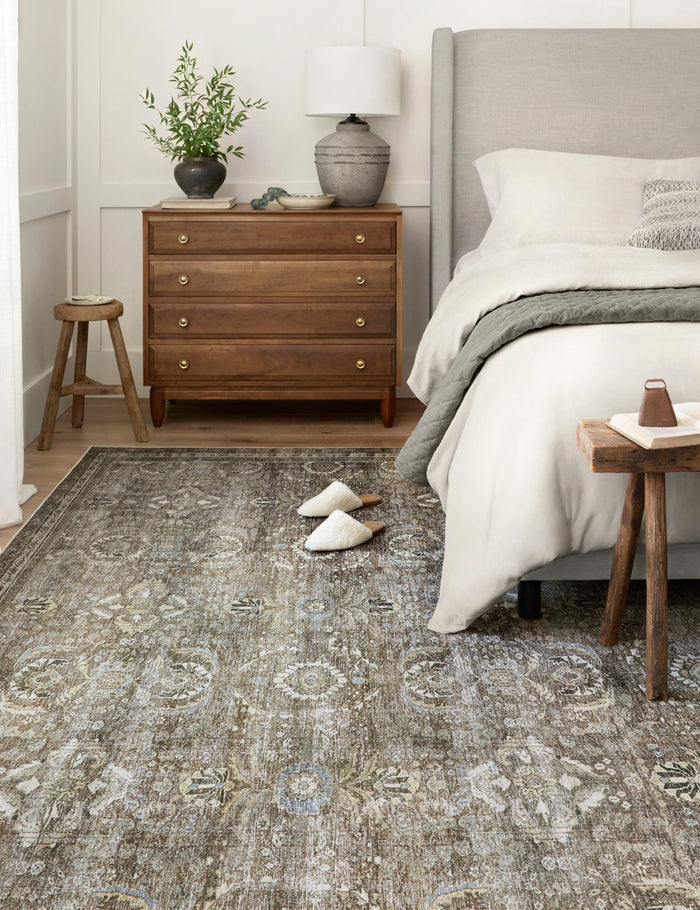 #color::antique-and-moss #size::2--x-5- #size::2-3--x-3-9- #size::2-6--x-7-6- #size::2-6--x-9-6- #size::2-6--x-12- #size::3-6--x-5-6- #size::5--x-7-6- #size::7-6--x-9-6- #size::9--x-12- | Amalia distressed traditional rug lays under a gray linen framed bed in a bedroom with a wooden bedside dresser, stool, and bench