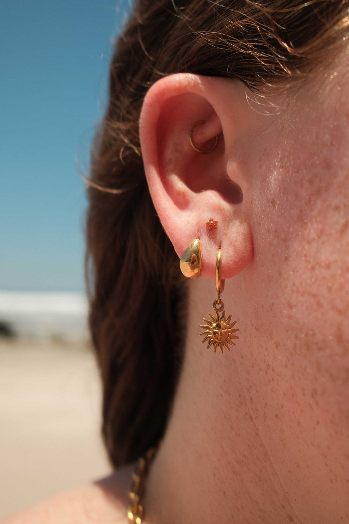 Close-up of an ear with gold hoop earrings and an orange floral-shaped flat back stud.