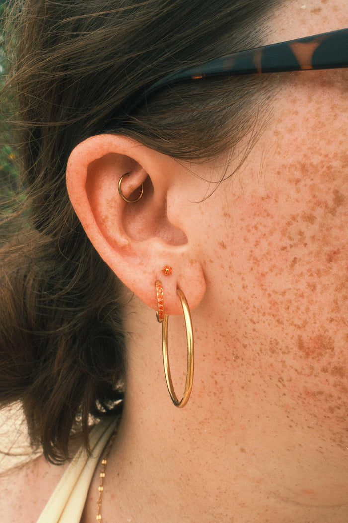 Close-up of an ear with gold hoop earrings and an orange floral-shaped flat back stud.