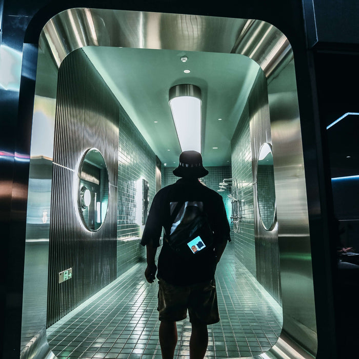 Divoom Sling Bag Pixel Art LED Daypack, a person wearing the bag in a sleek neon-lit tiled hallway with a blue and orange pixel display, smartphone app controlled, nightlife decor