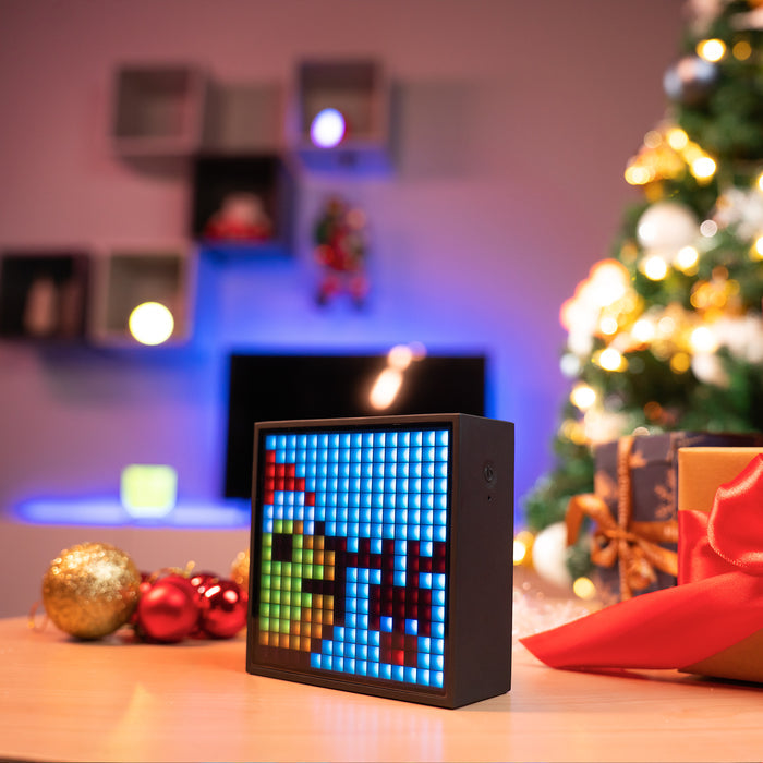 Divoom Timebox-Evo Pixel Art Speaker 16x16 DIY LED Display Alarm Clock Box, colorful pixel holiday art beside gifts and a lit Christmas tree, audio speaker, festive living room decor