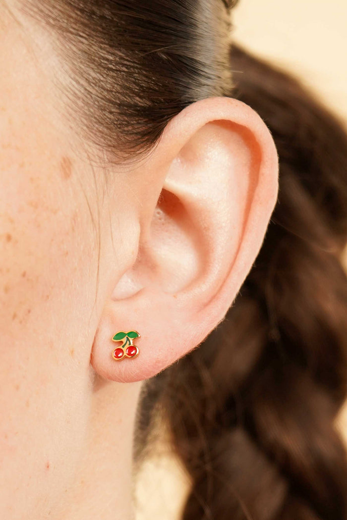 Close-up of an ear wearing a colorful enamel and gold double cherry flat back stud earring with a blurred background