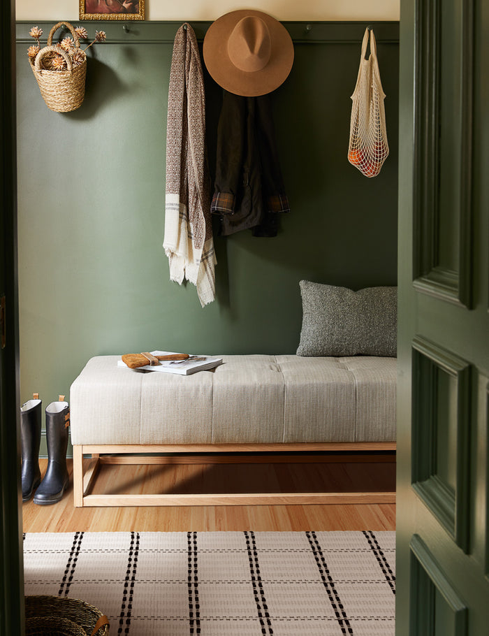 #size::1-9--x-2-10- #size::2--x-5- | Elin mat lays on a hardwood floor in an entry way with green walls, a gray cushioned bench, and a gray throw pillow