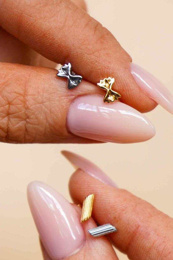 Close-up of a hand holding multiple gold and silver flat back stud earrings that are shaped like different pasta noodles.