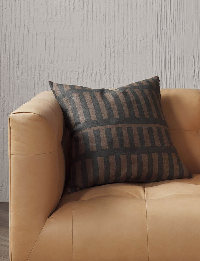 #size::20--x-20- | Kellan square throw pillow sits on a light brown leather sofa in a studio room with textured walls