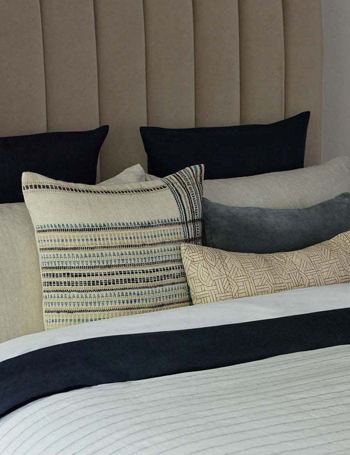 #size::12--x-20- | The Kisha natural-toned lumbar throw pillow sits on a beige velvet framed bed with blue and ivory linens