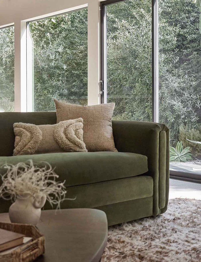#size::12--x-20- #size::20--x-20- | The Kisha natural-toned square throw pillow sits on a green velvet sofa with a plush ivory throw pillow