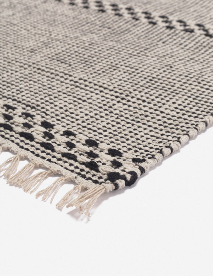 #size::1-9--x-2-10- #size::2--x-5- | Corner shot of the Masha gray and black geometric machine washable mat with tasseled ends
