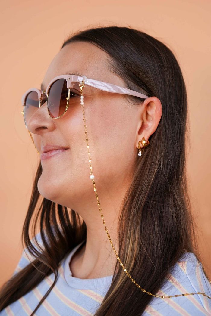 Woman wearing sunglasses with a gold chain, against a beige background