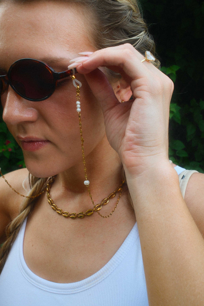 Woman wearing sunglasses with a long gold chain.