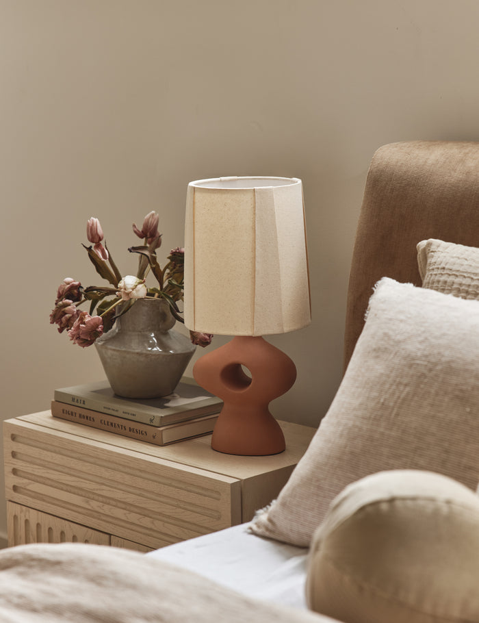 #color::clay  | Rhodes sculptural ceramic table lamp styled on a nightstand in a bedroom.