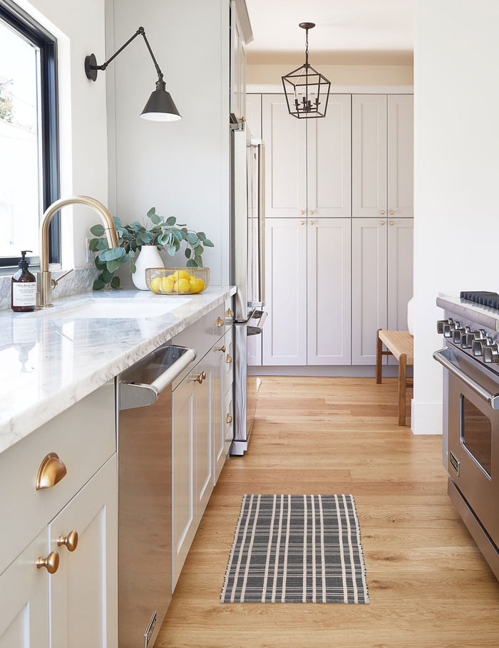 #size::1-9--x-2-10- #size::2--x-5- | The Rika black and white cotton machine washable mat with checkerboard pattern in its runner size lays in a kitchen with marble countertops