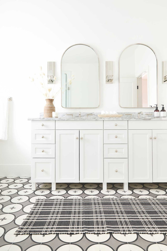 #size::1-9--x-2-10- #size::2--x-5- | The Rika black and white cotton machine washable mat with checkerboard pattern in its runner size lays in a bathroom with two silver framed mirrors