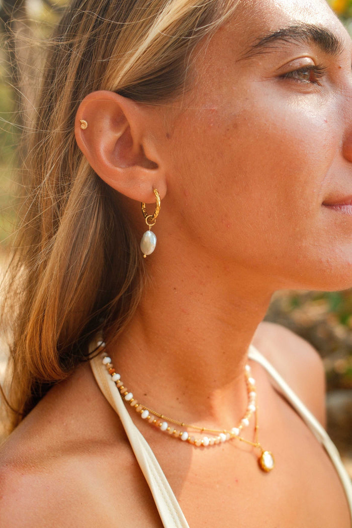 Close-up of a woman wearing gold earrings and a necklace with a blurred natural background