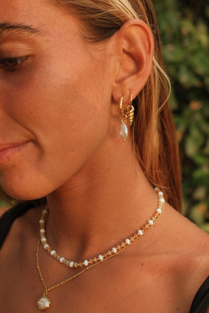 Close-up of a woman wearing gold hoop earrings and pearl necklaces with a blurred green background