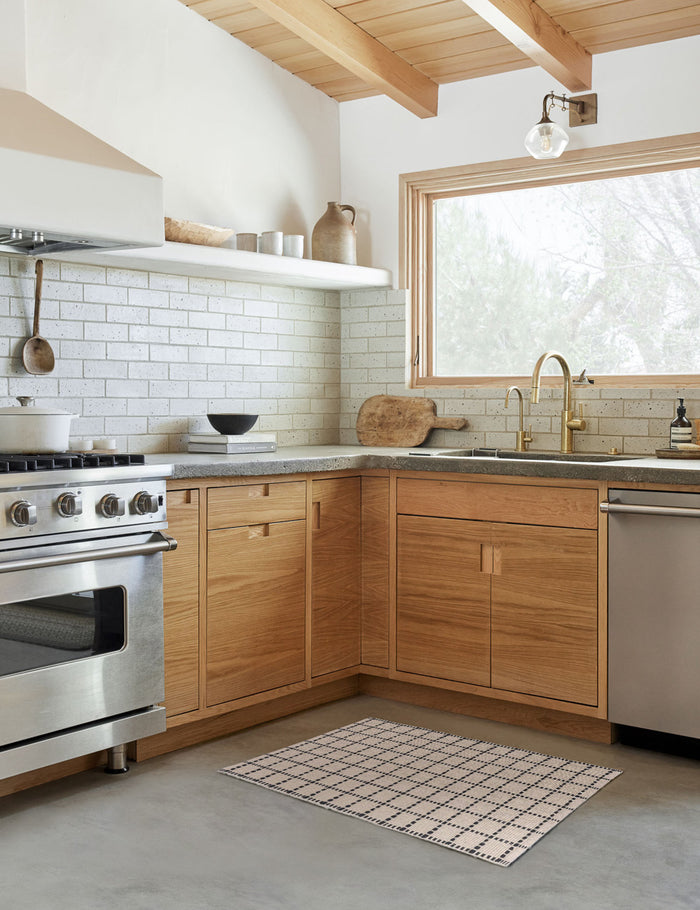 #size::1-9--x-2-10- #size::2--x-5- | The Sebou natural and black dotted machine washable mat lays in a kitchen with a subway tile backsplash and wooden cabinetry