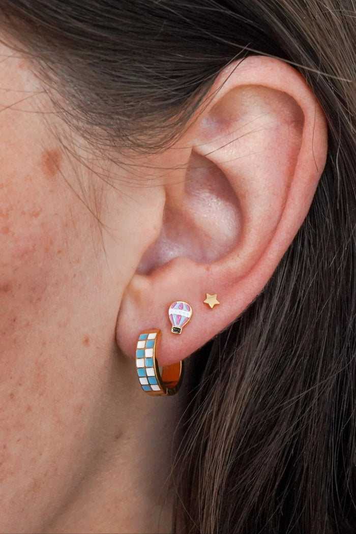 Close-up of an ear wearing colorful hoop earrings with a star and hot air balloon design.