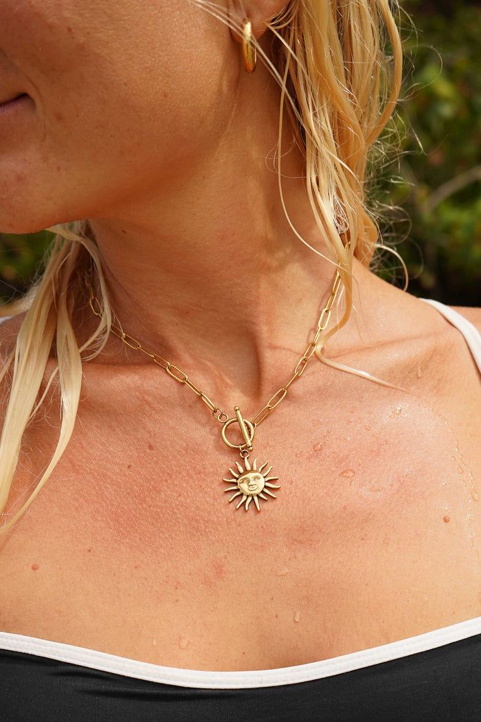 Close-up of a person wearing a gold necklace with a sun pendant.