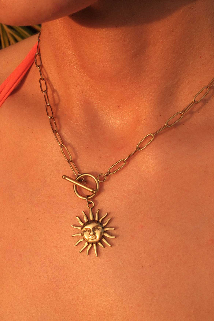Gold necklace with a sun pendant on a person's neck