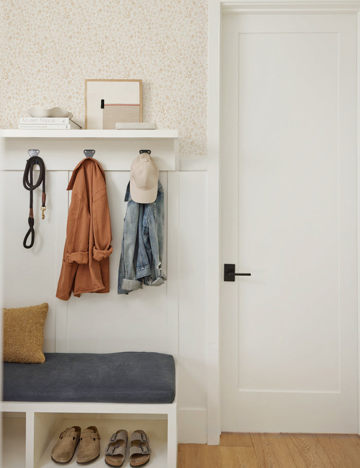 #color::goldenrod | The sommerville goldenrod wallpaper is in an entry room with a hanging coat rack and a white bench with blue cushioning