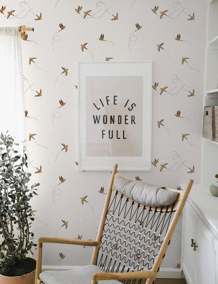 #color::rust | The Sparrow brown wallpaper by Rylee and Cru is in a room with a graphic wall art mounted against it behind a natural vase and a woven rocking chair with gray cushioning.