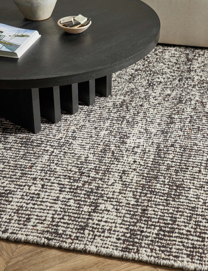 #color::espresso #size::10--x-14- #size::2-6--x-8- #size::6--x-9- #size::8--x-10- #size::9--x-12- #size::12--x-15- | Close up of the Taos espresso rug laying in a living room under a round coffee table and an ivory sectional