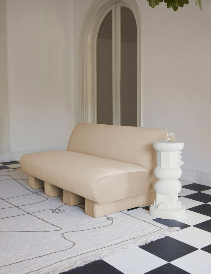 #size::short | The toivo short pedestal stands next to a beige velvet sofa on top of a checkerboard floor