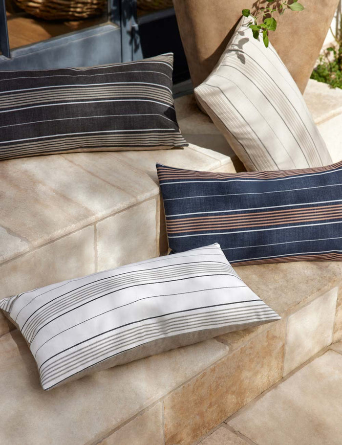 #size::12--x-22- | The whitehaven indoor and outdoor pillow lays on a stone staircase outside with the other colors of the whitehaven pillow
